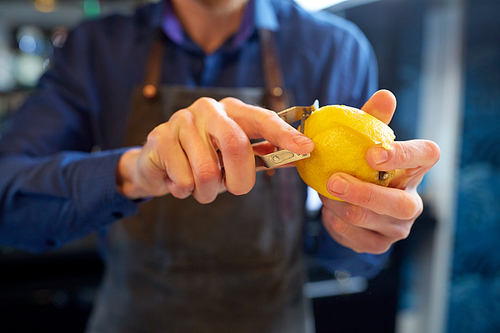 people and profession concept - bartender with peeler removing peel from lemon at bar