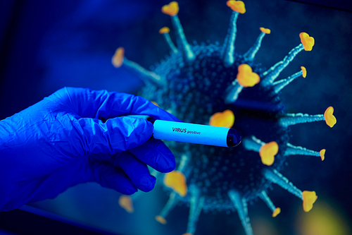 medicine, healthcare and science concept - close up of hand in protective medical glove holding beaker with virus positive blood test over coronavirus on background