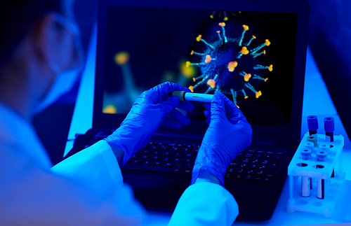 medicine, healthcare and science concept - close up of hand in protective medical glove holding beaker with virus positive blood test over coronavirus on laptop computer screen at laboratory