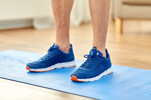 fitness, sport and footwear concept - close up of male feet in blue sneakers on exercise mat