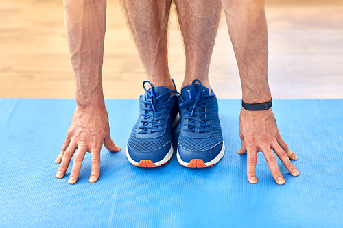 fitness, sport and footwear concept - close up of male hands and feet in blue sneakers on exercise mat