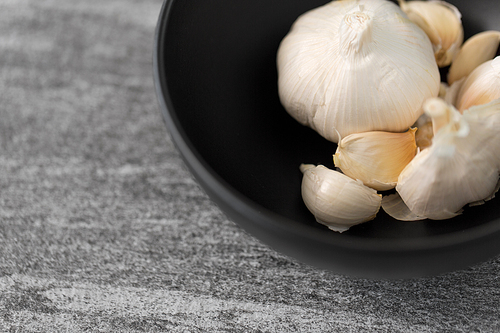 vegetable, food and culinary concept - garlic in bowl on slate stone background