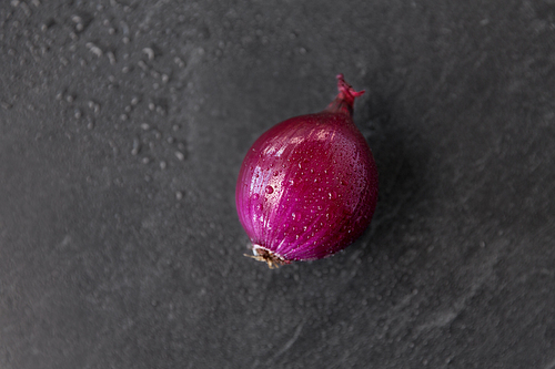 vegetable, food and culinary concept - red onion on wet slate stone background