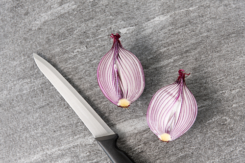 vegetable, food and culinary concept - red onion cut in half and kitchen knife on slate stone background