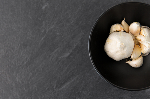 vegetable, food and culinary concept - garlic in bowl on slate stone background