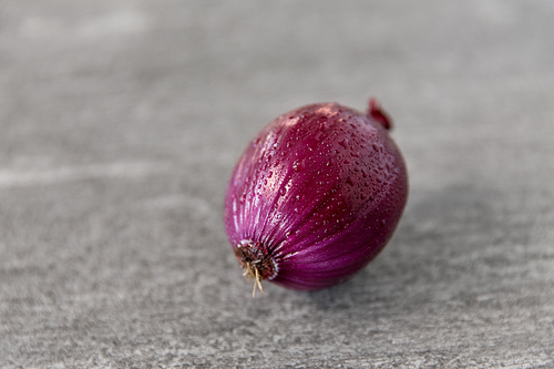 vegetable, food and culinary concept - close up of wet red onion on slate stone background