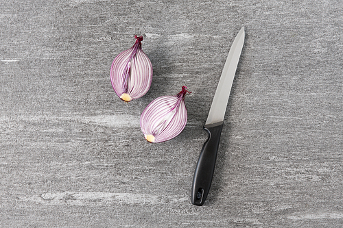 vegetable, food and culinary concept - red onion cut in half and kitchen knife on slate stone background