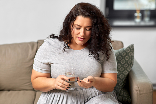 people, health and treatment concept - young woman taking medicine pills with water at home