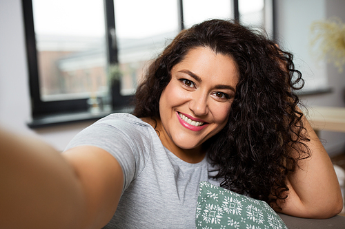 people, technology and leisure concept - happy smiling young woman taking selfie at home