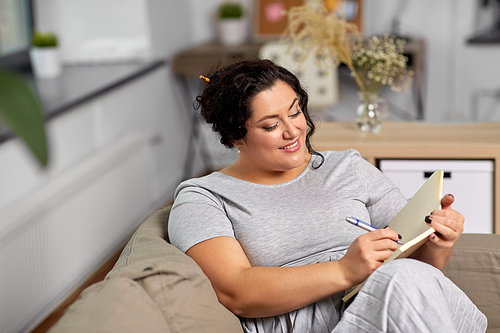 people and leisure concept - happy young woman with diary and pen taking notes on sofa at home