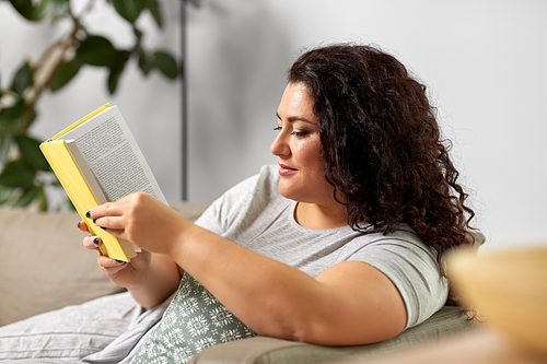 people and leisure concept - young woman reading book on sofa at home