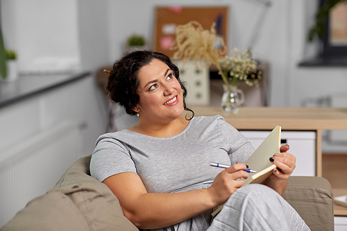 people and leisure concept - happy young woman with diary and pen taking notes on sofa at home