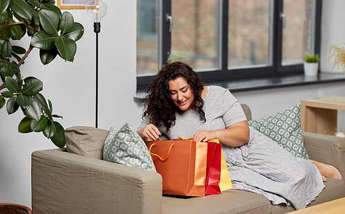 consumerism, people and sale concept - happy smiling young woman with shopping bags on sofa at home