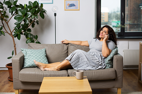 communication, people and leisure concept - happy young woman calling on smartphone on sofa at home