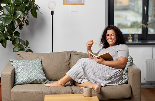 people and leisure concept - happy young woman with diary and pencil on sofa at home