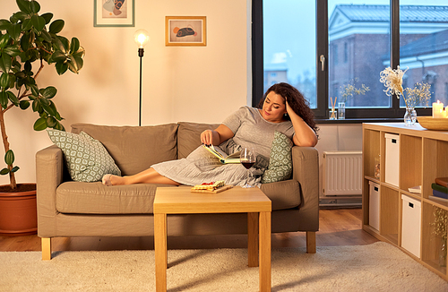 leisure and people concept - woman reading book with red wine and snacks on table at home in evening