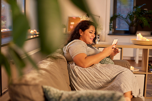 technology, leisure and people concept - happy smiling woman with smartphone at home in evening