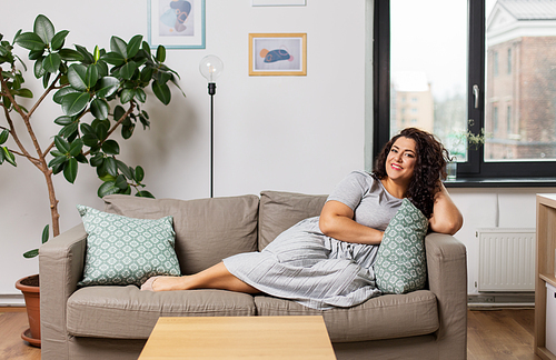 people and leisure concept - happy young woman lying on sofa at home