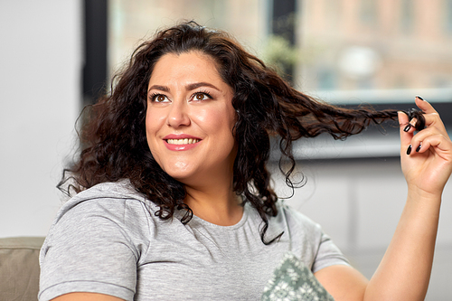 people and leisure concept - portrait of happy young woman playing with her hair strand at home