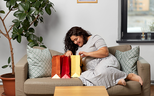 consumerism, people and sale concept - happy smiling young woman with shopping bags on sofa at home