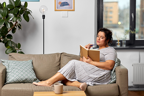 people and leisure concept - young woman with diary and pencil taking notes on sofa at home