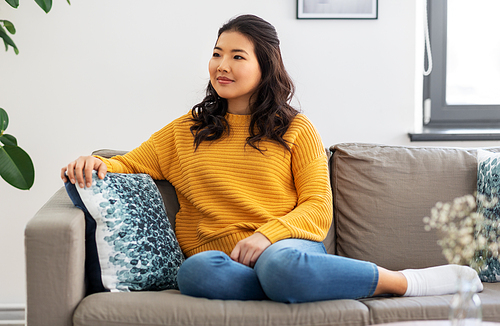 people and leisure concept - asian young woman in yellow sweater sitting on sofa at home