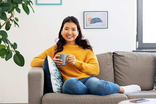 people and leisure concept - happy smiling asian young woman in earphones listening to music and drinking coffee at home