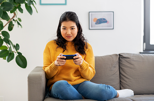 people and leisure concept - asian young woman with gamepad playing video game at home