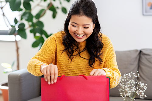 people and leisure concept - happy smiling asian young woman in yellow sweater with shopping bag sitting on sofa at home