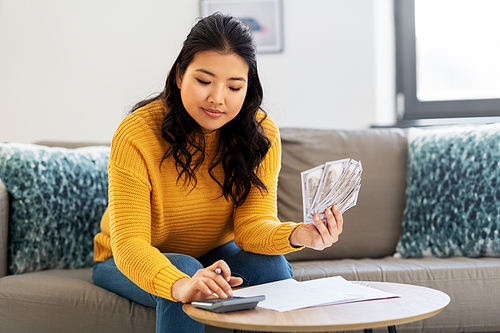 accounting, taxes and finances concept - young asian woman with papers and calculator counting money at home