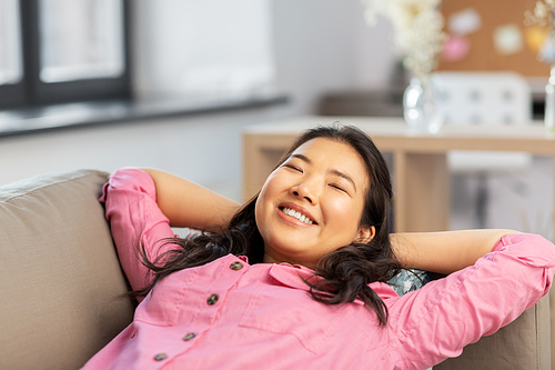 people and leisure concept - happy smiling asian young woman in pink shirt lying on sofa and dreaming at home