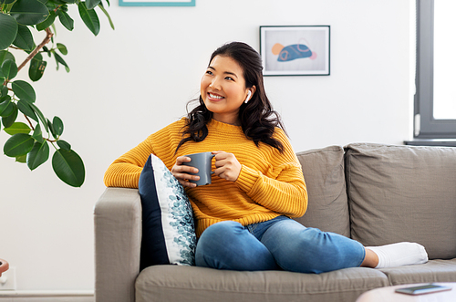 people and leisure concept - happy smiling asian young woman in earphones listening to music and drinking coffee at home