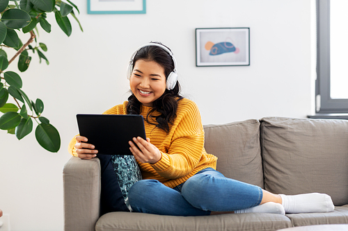 people and leisure concept - happy smiling asian young woman in headphones listening to music on tablet pc computer at home