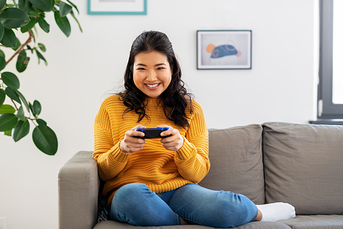 people and leisure concept - happy smiling asian young woman with gamepad playing video game at home