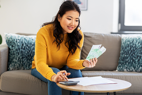 accounting, taxes and finances concept - young asian woman with papers and calculator counting money at home