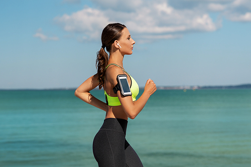 fitness, sport and healthy lifestyle concept - young woman with earphones and smartphone running outdoors