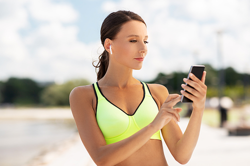fitness, sport and healthy lifestyle concept - young woman with earphones and smartphone exercising outdoors