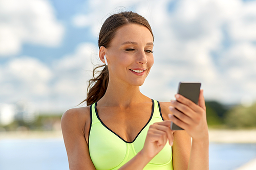 fitness, sport and healthy lifestyle concept - happy smiling young woman with earphones and smartphone exercising outdoors