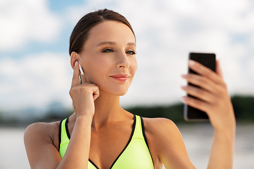 fitness, sport and healthy lifestyle concept - young woman with earphones and smartphone exercising outdoors