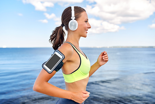 fitness, sport and healthy lifestyle concept - happy smiling young woman in headphones with smartphone running outdoors