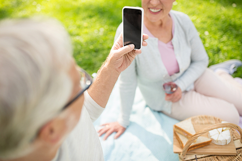 old age, leisure and technology concept - close up of happy senior couple having picnic and taking picture by smartphone at summer park