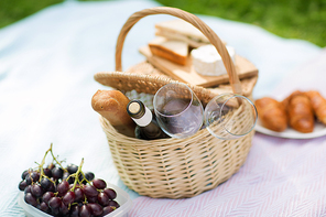 leisure concept - picnic basket, food and wine glasses on blanket at summer park