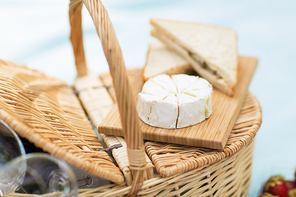 food, eating and leisure concept - brie or camembert cheese and sandwiches on wicker picnic basket