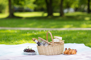leisure concept - picnic basket, food and wine glasses on blanket at summer park