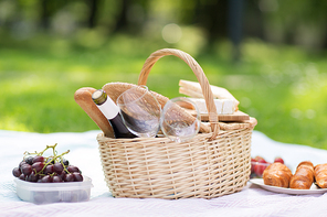 leisure concept - picnic basket, food and wine glasses on blanket at summer park