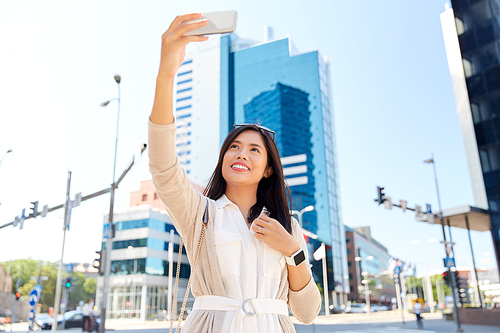 communication, lifestyle and technology concept - smiling young asian woman taking selfie by smartphone on city street