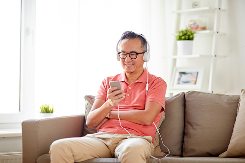 technology, people and lifestyle concept - happy man with smartphone and headphones listening to music at home