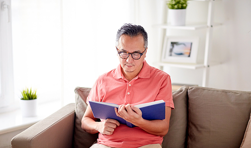 leisure, literature and people concept - man sitting on sofa and reading book at home