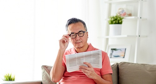 leisure, information, people and mass media concept - happy man in glasses reading newspaper at home