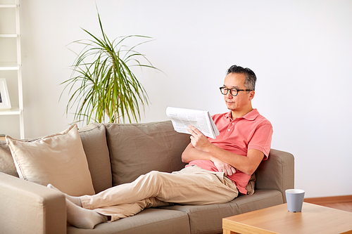 leisure, information, people and mass media concept - happy man in glasses reading newspaper at home